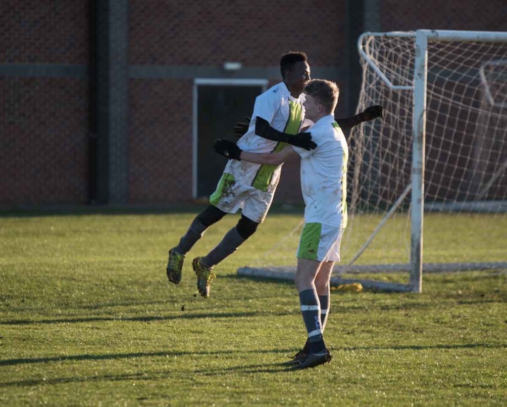 Two football players embrace after scoring a goal on a sunlit field