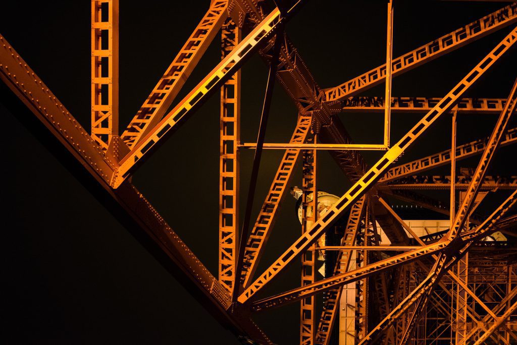 An abstract view of metal girders designed as a structural frame, lit by an orange sidelight