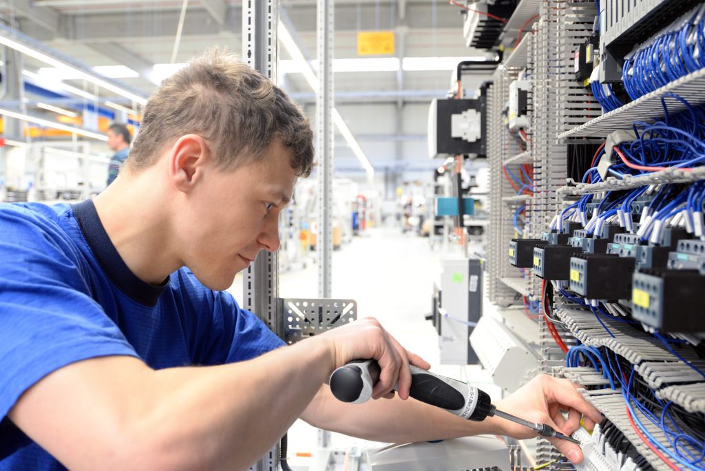 young apprentice assembles components and cables in a factory in a switch cabinet - workplace industry with future