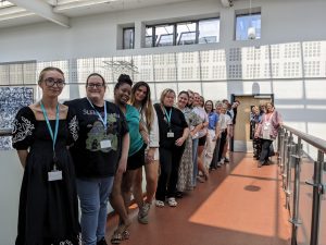 20 female and male students and staff stood on a balcony in a row looking towards the camera.