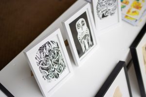 A shelf displaying small framed black‑and‑white linocut‑style prints of stylised faces with bold carved lines.